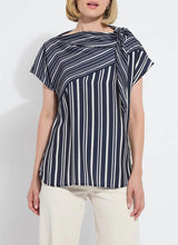 Load image into Gallery viewer, The Tamar Stripe Bow-Tie Neck Top is a standout piece, designed in a nautical collage color with distinctive stripes for a timeless, chic appeal. Made from premium Lightweight Satin, this top offers a luxurious feel while maintaining effortless wearability. Its relaxed, boxy fit is complemented by stylish details like a bow tied to one shoulder and a rounded, high-low shirttail hem. Perfect for casual yet polished ensembles, the Tamar Stripe Bow-Tie Neck Top is a versatile addition.