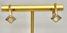 Load image into Gallery viewer, A pair of gold hoop earrings with diamond-shaped bezel-set moonstones, displayed on a gold T-bar stand against a light gray background.