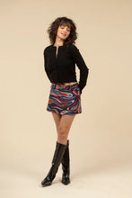 Load image into Gallery viewer, Woman wearing a black sweater, tall black boots and mini skort in abstract pattern against a white background.