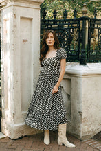 Load image into Gallery viewer, Woman in a brown and white polka dot dress and white boots, standing outdoors near classical architecture.