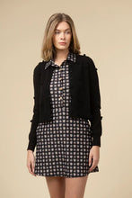 Load image into Gallery viewer, Woman wearing a black cardigan over a patterned dress against a beige background.