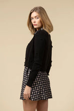 Load image into Gallery viewer, Woman wearing a black cardigan and patterned dress against a beige background.