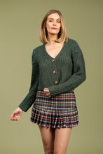 Load image into Gallery viewer, Woman wearing a green cardigan, multi-color plaid skirt against a pale green background.