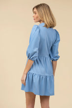 Load image into Gallery viewer, Woman wearing a blue dress with puff sleeves against a beige background.