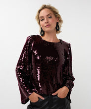 Load image into Gallery viewer, Woman wearing a sequined maroon flared sleeve blouse, large black oval drop earrings and black pants standing against a brick wall.