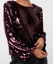 Load image into Gallery viewer, Woman wearing a sequined maroon flared sleeve blouse and black pants standing against a white wall.
