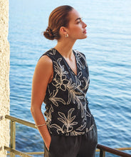 Load image into Gallery viewer, Woman wearing a black sleeveless top with off-white floral embroidery and black pants standing on a deck overlooking the water.