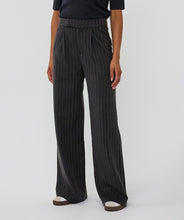 Load image into Gallery viewer, Model wearing black pinstripe pants, black short sleeve top and white and black sneakers against a white background.