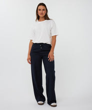 Load image into Gallery viewer, Woman wearing a white top, navy pinstripe pants and white sneakers against a white background.