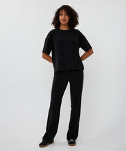 Load image into Gallery viewer, Woman wearing a black short sleeve top, black pants and black sneakers against a white background.