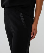Load image into Gallery viewer, Black pants with a satin design on pocket against a plain background.