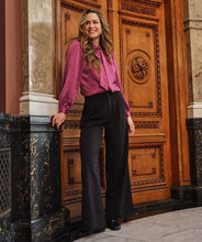 Load image into Gallery viewer, Woman in a pink blouse, black pants with glittering studs and black shoes standing in front of an ornate wooden door.