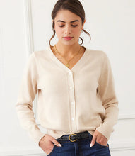 Load image into Gallery viewer, Woman wearing a beige cardigan, blue jeans, heart necklace and black belt against a white wall.