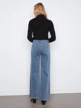 Load image into Gallery viewer, A woman viewed from behind wearing a black ribbed turtleneck sweater and high-waisted, wide-leg blue denim jeans, standing against a plain white wall.