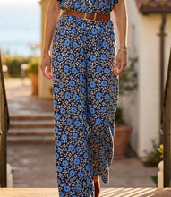 Load image into Gallery viewer, Model wearing a blue floral wide leg pant, brown belt and brown sandals walking outside.