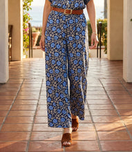 Load image into Gallery viewer, Model wearing a blue floral wide leg pant, brown belt and brown sandals walking on a tiled patio.
