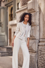 Load image into Gallery viewer, Woman wearing a white sparkle top, white sparkle jacket and white pants leaning against a stone wall.