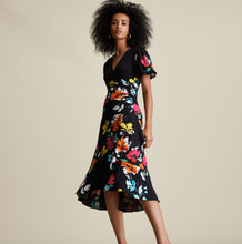 Load image into Gallery viewer, Joseph Ribkoff is known for modern and stylish pieces that are beyond gorgeous and this Aria dress fits all of those qualities and more! A striking floral pattern in various shades of blue, white, orange, yellow and red comes alive on a beautiful black background. A beautiful V-neck is highlighted with a crossover design leading to rouching at the side. A billowy sleeve adds to the attractiveness. For so many dazzling moments in your life, this is the dress of choice!