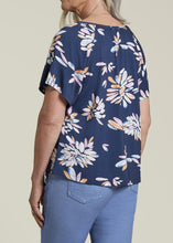 Load image into Gallery viewer, A woman wearing a navy blue scoop neck top with a floral pattern in pinks, blues, and coral, paired with blue jeans.