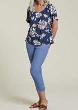 Load image into Gallery viewer, A woman wearing a navy blue scoop neck top with a floral pattern in pinks, blues, and coral, paired with blue jeans.