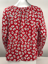 Load image into Gallery viewer, Small white flowers with black centers just pop on this gorgeous true red long sleeve top. The feminine touches create a romantic top with a scoop neckline and a row of button closures, as well as ruffled cuffs. A lightweight material, this will keep you cool in the warmer days and warm when there is a slight chill. This is the choice of top to pair with crisp white bottoms and effortlessly goes well with jeans.