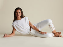 Load image into Gallery viewer, This slim leg capri designed by Joseph Ribkoff has a style that is not only unique but highly fashionable. The floral cut-out pattern at the cuff of each leg is enhanced by sparkling crystals that catch the eye! A slight fray at the bottom of each leg gives this spectacular jean an edge. The Isla is not only elegant but also fun at the same time. A pure white jean, this capri will pair beautifully with anything in your closet!