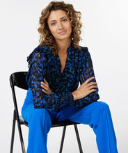 Load image into Gallery viewer, A gorgeous pop of all over blue in an animal print is striking on the Wilda Wild Celebration Blouse. The Wilda has a round neckline, decorative ruffles on the shoulders and smocked cuffs. Pair with a pair of faux leather or black pants or your favorite denim and boots and you'll be a fashionista!