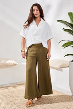 Load image into Gallery viewer, Woman wearing a white blouse and olive green wide-leg pants in a bright room with a plant.

