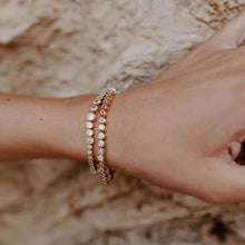 Load image into Gallery viewer, A graduated silhouette modernizes a classic tennis bracelet. Plated in 14-karat gold and lined with cubic zirconia, this sparkling piece of jewelry is an eye catcher and compliment maker.  Our Alexandria Graduated Bracelet matches perfectly with our Alexandria Graduated Tennis Necklace.  Color- Gold and Clear. 7 inch. 14 kt gold over brass.
