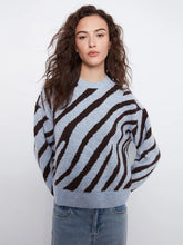 Load image into Gallery viewer, A woman wearing a light blue and dark brown zebra-striped knit sweater with blue jeans, photographed against a plain light gray studio background.

