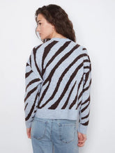 Load image into Gallery viewer, A woman shown from the back wearing a light blue and dark brown zebra-striped knit sweater with light-wash blue jeans, set against a plain white studio background.
