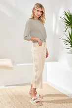 Load image into Gallery viewer, Woman wearing a striped sweater, beige pants and sandals in a bright room with a plant.
