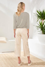Load image into Gallery viewer, Woman wearing a striped shirt, beige pants and sandals in a bright room with a plant.
