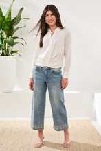 Load image into Gallery viewer, Woman wearing a white blouse, blue jeans with embellishments and sandals standing in a room with a plant and white wall.
