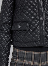 Load image into Gallery viewer, Close-up of the pocket and hem on the black quilted jacket.
