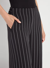 Load image into Gallery viewer, Close-up of black pinstripe pants worn by a model on a gray background.
