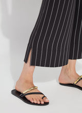 Load image into Gallery viewer, Model wearing black sandals with gold straps and black pants with white stripes on a white background.
