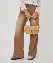Load image into Gallery viewer, Person wearing brown pants and a white lace top, holding a woven handbag on a plain background.
