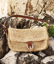 Load image into Gallery viewer, Woven handbag with brown leather accents and gold buckle sitting on a stone surface.

