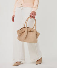 Load image into Gallery viewer, Model wearing a peach sweater, white pants and beige heels, carrying a cappuccino colored suede bag against a white background.
