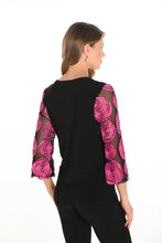 Load image into Gallery viewer, Woman wearing a black top with pink begonia patterns on sleeves and black pants against a white background. 
