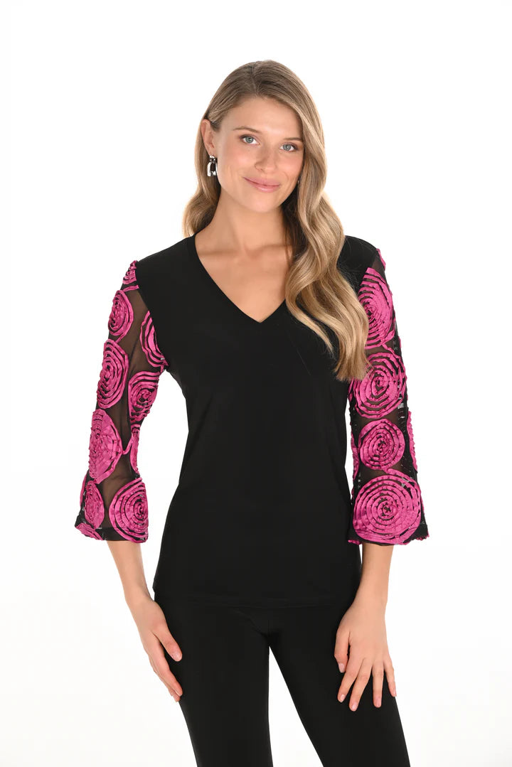 Woman wearing a black top with pink begonia patterns on sleeves and black pants against a white background. 