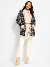 Load image into Gallery viewer, Woman wearing a neutal and black long jacket over a neutral riding sweater and white pants and suede beige boots against a white background.
