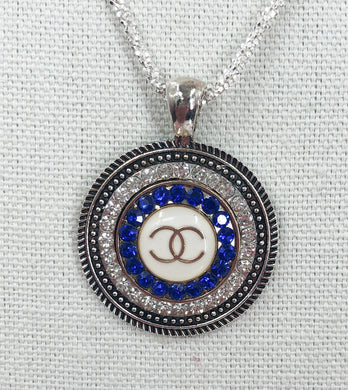 A stunning blue Coco Chanel button with gold lettering fancifully sits in a gorgeous sparkling silver base with twinkling crystals.  This brilliant pendant hangs beautifully from a sparkling 925 silver diamond cut chain and is a modern take on a vintage piece. This beauty you will be proud to show off! 