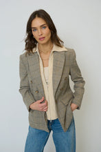 Load image into Gallery viewer, Woman wearing a plaid blazer over a cream shirt with blue jeans against a plain background.
