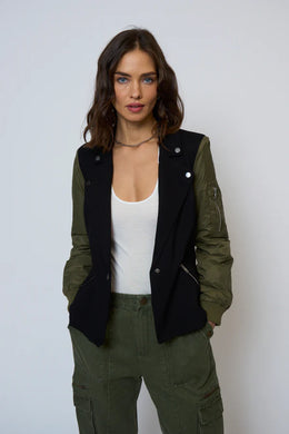 Woman wearing a black and green blazer over a white tank and green pants against a white background.