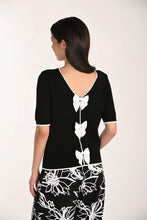 Load image into Gallery viewer, Woman wearing a black short sleeve top with white bows and floral pants on a plain background.
