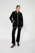 Load image into Gallery viewer, Woman wearing a black jacket with white trim, black pants and black boots against a white background.
