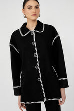 Load image into Gallery viewer, Woman wearing a black jacket with white trim and black pants against a white background.
