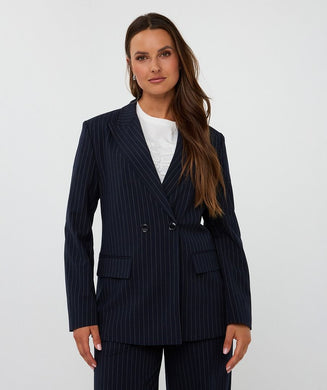 Woman wearing a navy pinstripe suit  and white top against a white background.